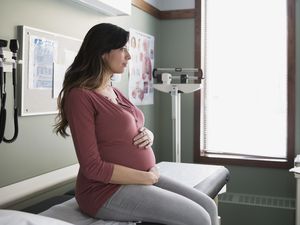 Pensive pregnant woman holding stomach in examination room