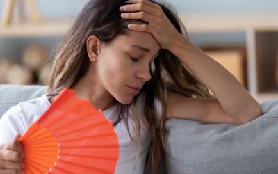 Close up woman sitting on couch reducing heat using fan