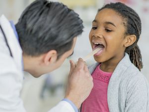 医生在观察一个小女孩的口腔时，用木制压舌器压住她的舌头