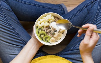 吃健康的早餐碗。酸奶、荞麦、种子、新鲜水果，放在女人手里的白色碗里。清洁饮食，节食排毒，素食理念