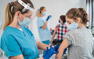 一个戴着口罩和面罩的护士给一个十几岁的女孩注射了一针。