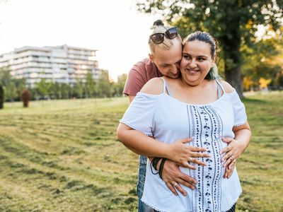 Cheerful overweight couple expressing romance in nature; pregnant obesity