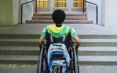 一位残疾学生站在学校门口。