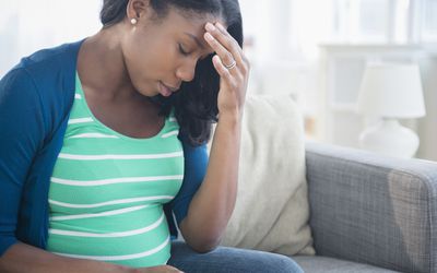焦虑的黑人孕妇在沙发上揉搓额头