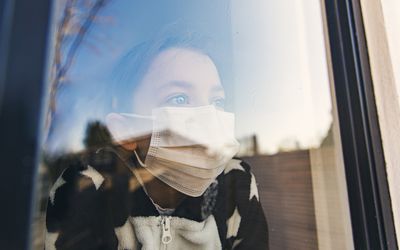 Little girl with covid-19 looks out a window