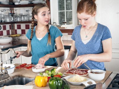 Teens making flatbread pizzas in kitchen