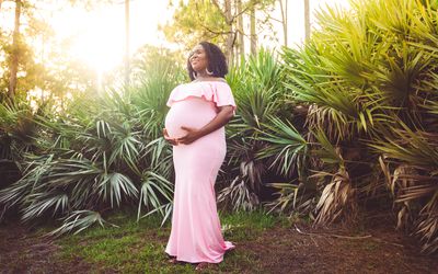 美丽发光的孕妇在粉红色的连衣裙摆姿势在户外的孕妇照片